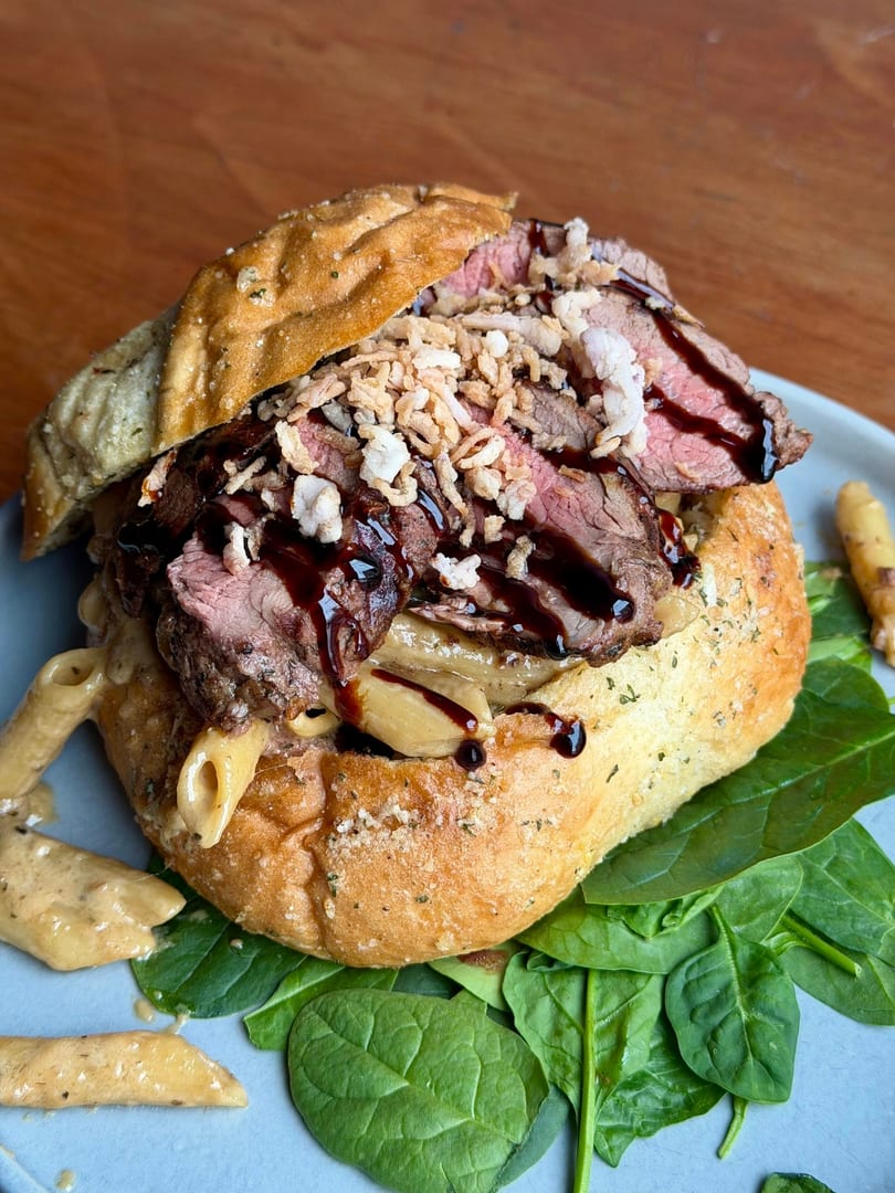 Savory bread bowl filled with steak, macaroni and cheese, crispy onions, and balsamic glaze.