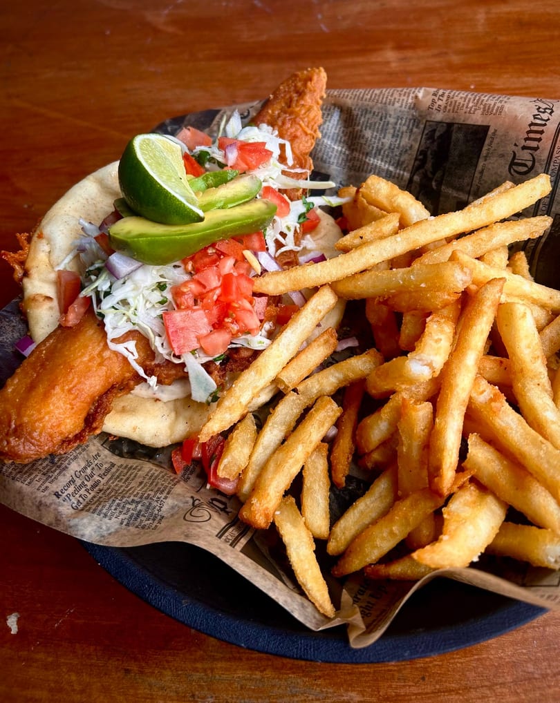 Crispy fish taco with avocado, lime, and salsa, served with a side of golden french fries.